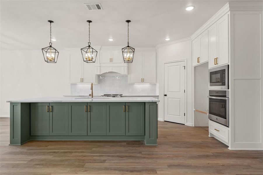 Kitchen featuring white cabinets, green cabinets, a kitchen island with sink, stainless steel appliances, and pendant lighting Kitchen featuring white cabinets, green cabinets, a kitchen island with sink, stainless steel appliances, and pendant lighting