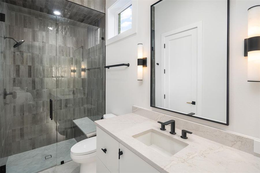 Luxuriously appointed ensuite bath to the first-floor secondary bedroom featuring an oversized walk-in shower with floor-to-ceiling upgraded tile, frameless glass enclosure, elegant quartz vanity, and striking designer light fixtures that elevate the space with a sophisticated, spa-like feel.