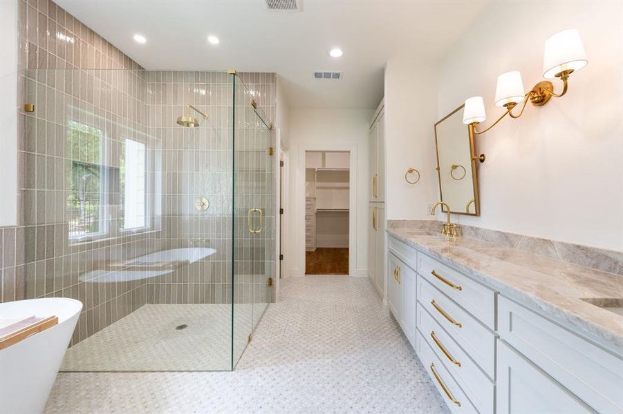Spacious bathroom featuring a frameless glass shower enclosure, a freestanding soaking tub, dual vanity with stone countertop, and custom cabinetry Spacious bathroom featuring a frameless glass shower enclosure, a freestanding soaking tub, dual vanity with stone countertop, and custom cabinetry
