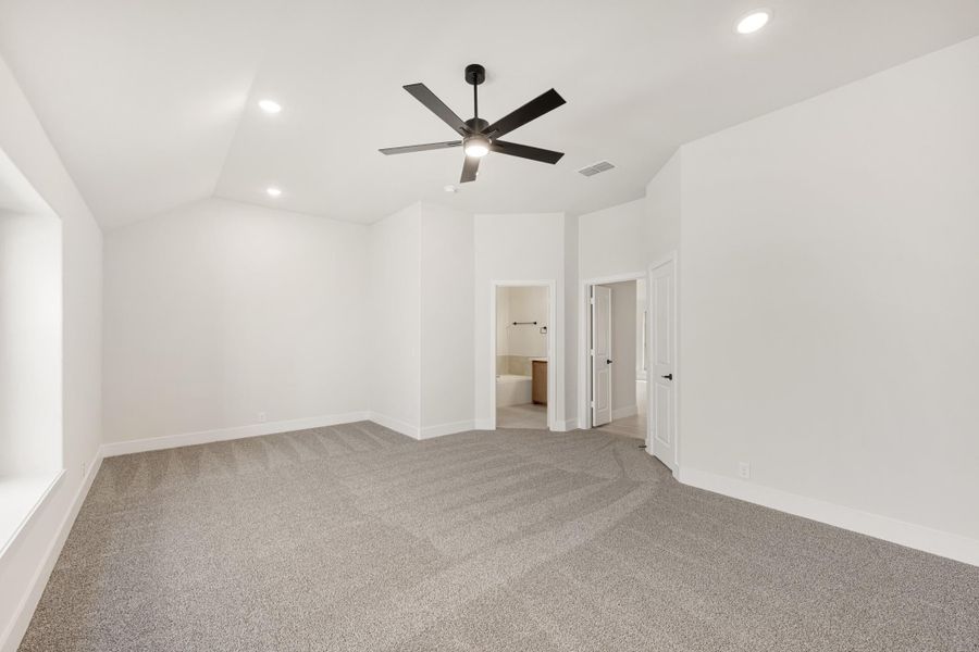 Empty master bedroom with vaulted ceiling, black ceiling fan, gray carpet, and ensuite bathroom doorway