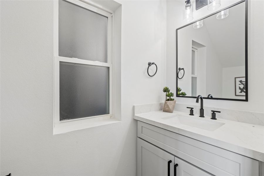 A beautifully designed vanity with ample storage, complemented by chic lighting and a frosted window for privacy and natural light.