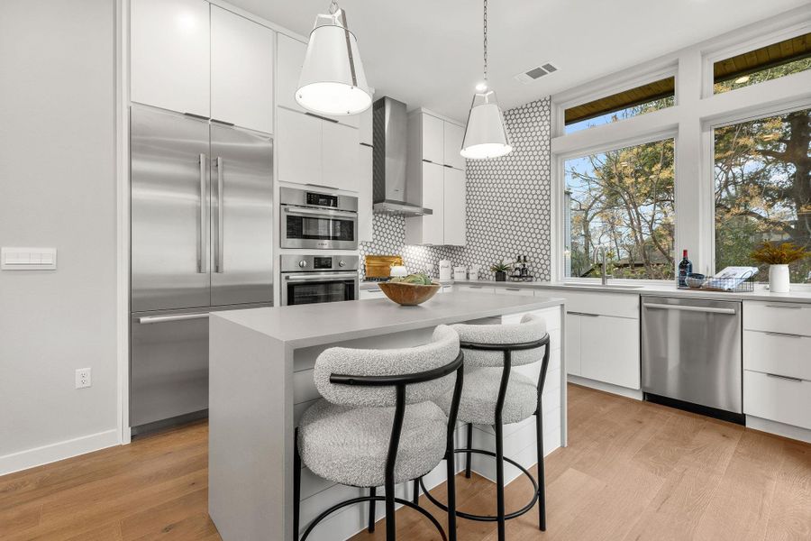 Kitchen with stainless steel appliances, white cabinetry, wall chimney exhaust hood, and modern cabinets