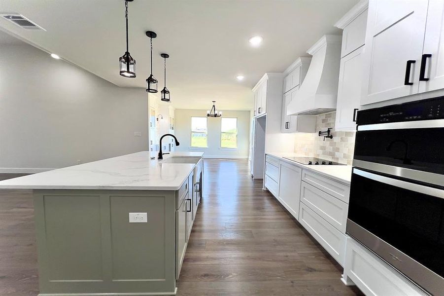 Kitchen with stainless steel double oven, dark floors, light stone counters, custom exhaust hood, and recessed lighting