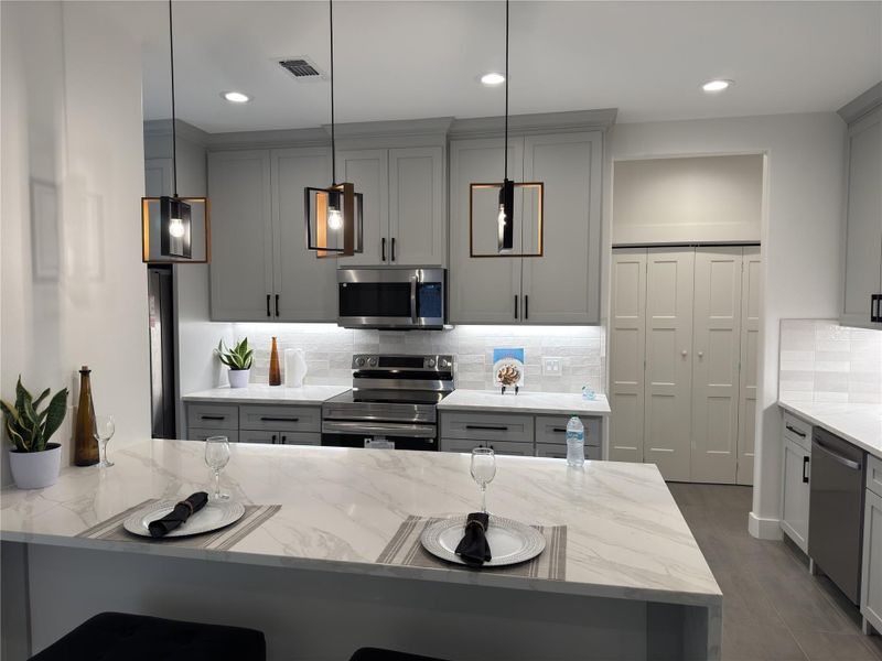 Kitchen with stainless steel appliances, gray cabinets, backsplash, light stone counters, and recessed lighting Kitchen with stainless steel appliances, gray cabinets, backsplash, light stone counters, and recessed lighting