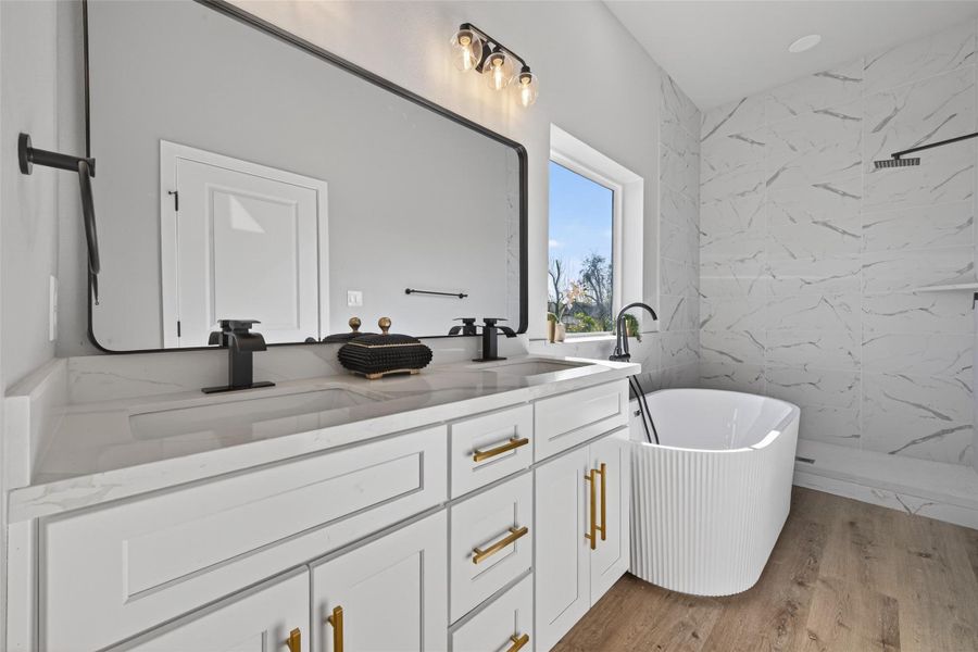Spa-inspired primary bathroom showcasing a custom double-sink quartz vanity with soft-close cabinetry, brushed gold hardware, matte black fixtures, oversized framed mirror, and elegant designer lighting.