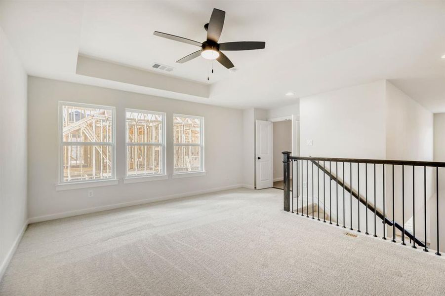 Spacious upper-level loft featuring light-toned carpeting, a contemporary ceiling fan, and a tray ceiling