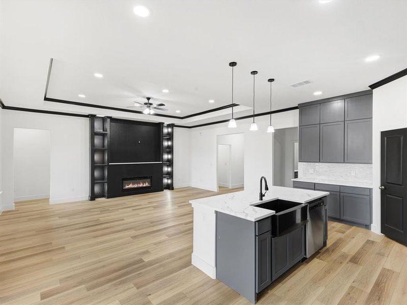 Kitchen featuring open floor plan, pendant lighting, gray cabinets, tasteful backsplash, and light wood-style floors Kitchen featuring open floor plan, pendant lighting, gray cabinets, tasteful backsplash, and light wood-style floors