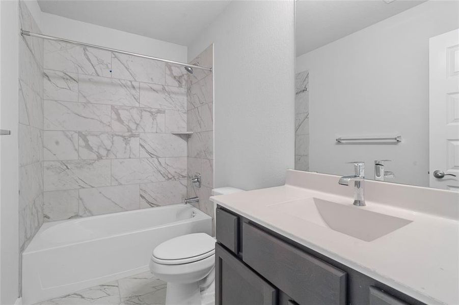 Secondary bath features tile flooring, bath/shower combo with tile surround, wood stained cabinets, beautiful light countertops, mirror, dark, sleek fixtures and modern finishes! This secondary bathroom has private access to a secondary bedroom.