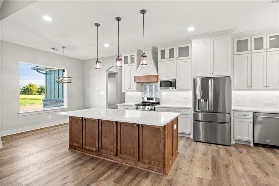 Kitchen with appliances with stainless steel finishes, white cabinets, decorative backsplash, decorative light fixtures, and glass insert cabinets Kitchen with appliances with stainless steel finishes, white cabinets, decorative backsplash, decorative light fixtures, and glass insert cabinets
