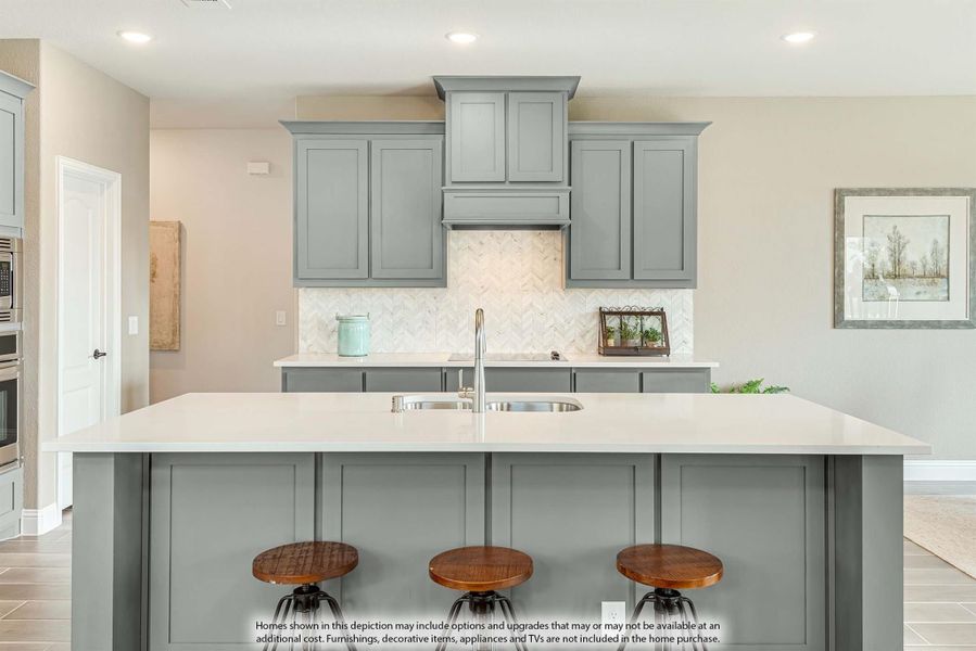 Kitchen with gray cabinets, herringbone tile backsplash, white island with sink, and three wood bar stools