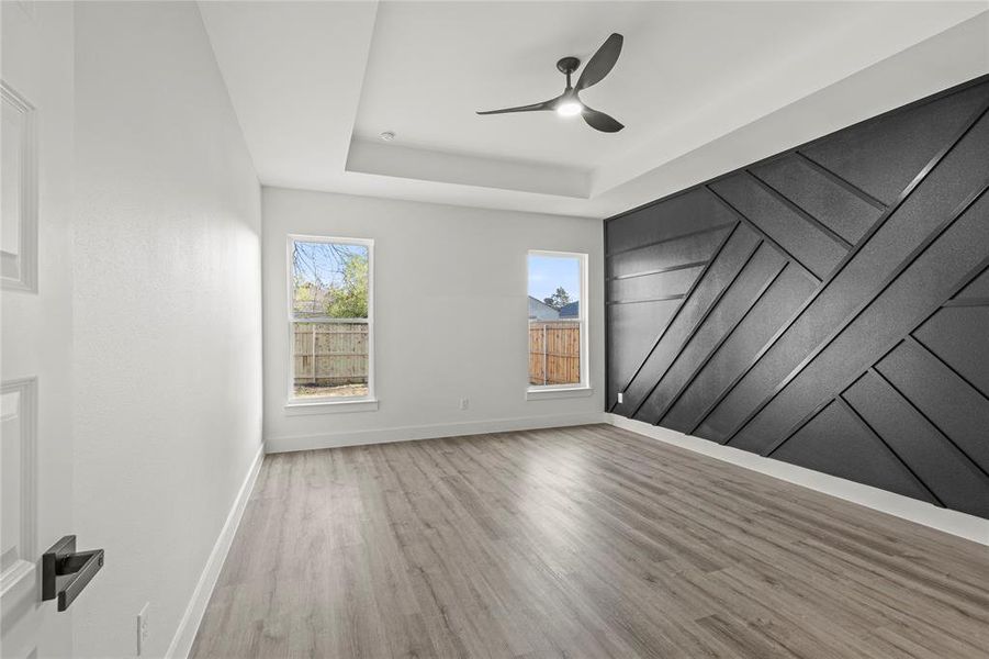 Spare room with a raised ceiling, ceiling fan, and light wood-type flooring