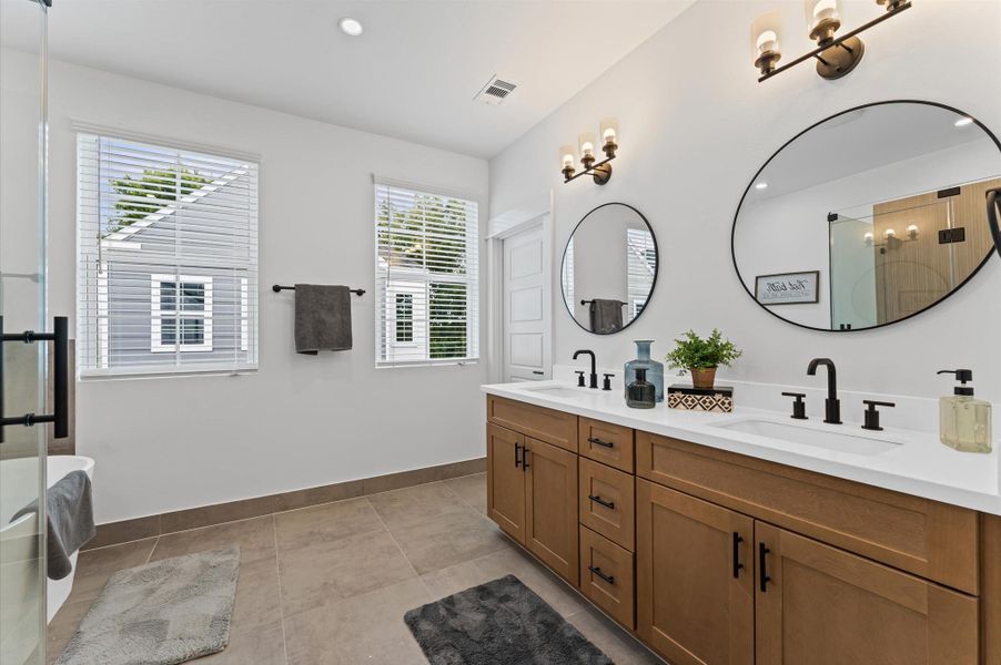 This luxurious primary bathroom blends modern elegance with spa-like comfort, featuring a spacious layout and contemporary selections throughout. A sleek double vanity with minimalist cabinetry and quartz countertops offers ample storage and style, while the glass-enclosed shower includes a built-in bench for added relaxation and convenience. The centerpiece is a sculptural freestanding soaking tub, perfectly positioned to invite unwinding after a long day.