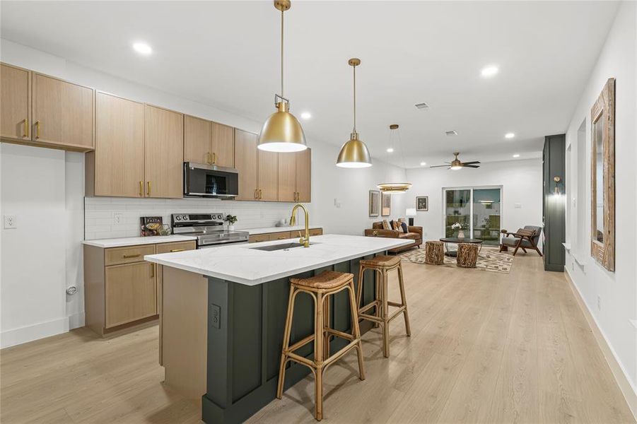 Kitchen featuring backsplash, decorative light fixtures, light stone countertops, stainless steel appliances, and light wood-style floors