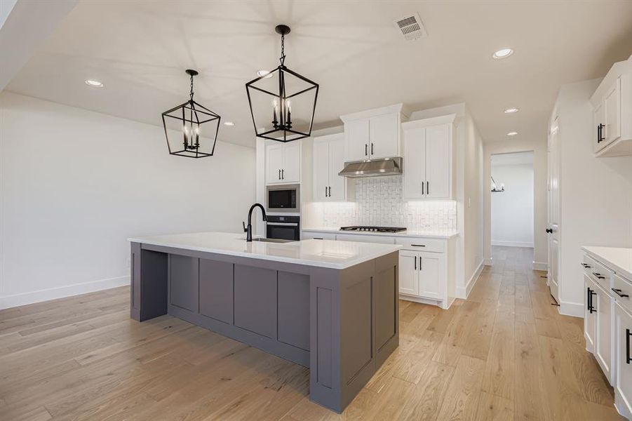 Kitchen with white cabinetry, gray cabinetry, a kitchen island with sink, hanging light fixtures, and tasteful backsplash