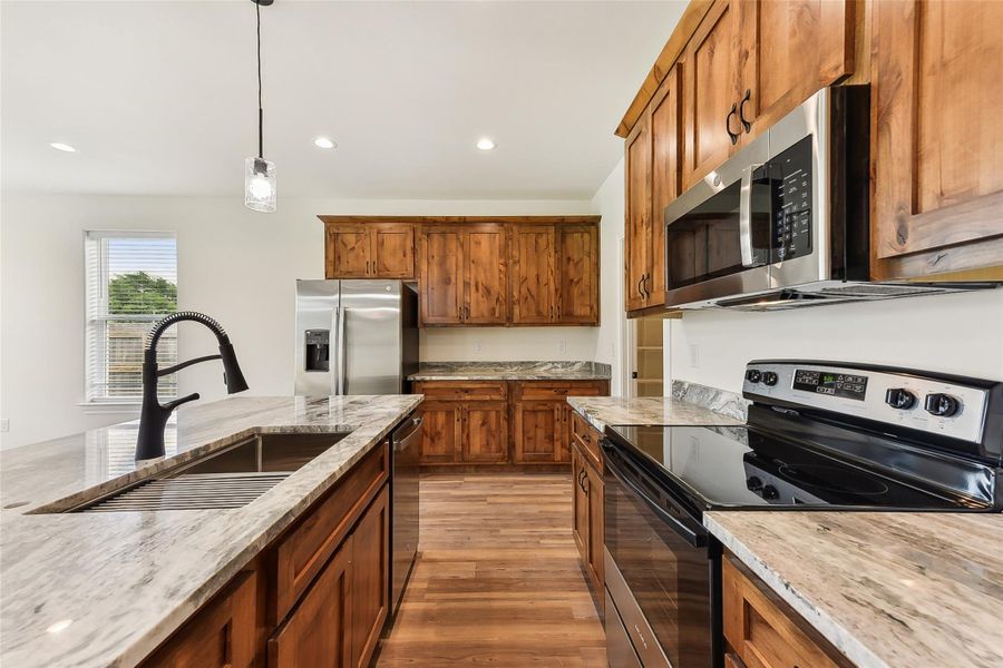 Kitchen with brown cabinets, a sink, light wood-style floors, light stone countertops, and appliances with stainless steel finishes Kitchen with brown cabinets, a sink, light wood-style floors, light stone countertops, and appliances with stainless steel finishes