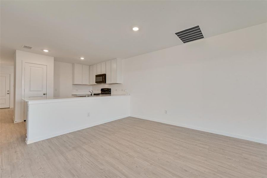 Kitchen with white cabinetry, sink, range, kitchen peninsula, and light hardwood / wood-style flooring