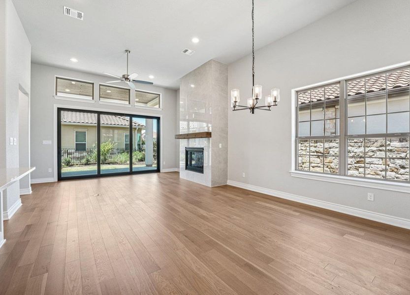 Unfurnished living room with hardwood / wood-style flooring, ceiling fan, a chandelier, a tiled fireplace, and recessed lighting