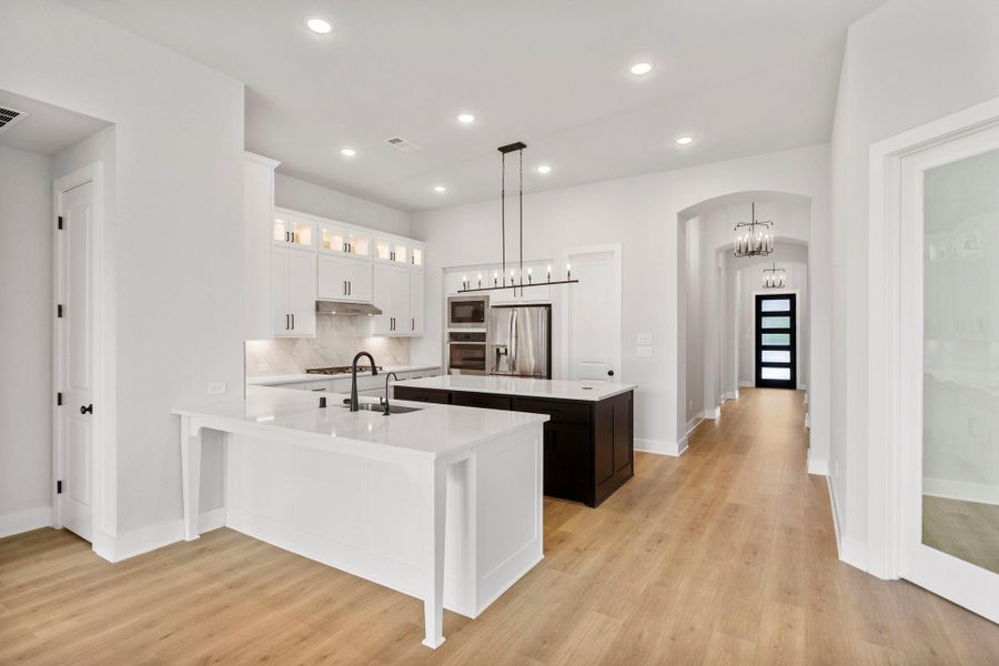Bright open kitchen with oversized quartz island, sleek cabinetry, recessed lighting, and warm hardwood floors.