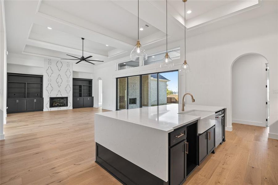 Kitchen with dark cabinetry, a raised ceiling, arched walkways, pendant lighting, and light wood-style flooring Kitchen with dark cabinetry, a raised ceiling, arched walkways, pendant lighting, and light wood-style flooring
