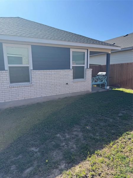 View of side of property with brick siding, roof with shingles, and a patio