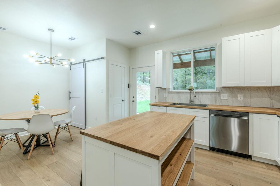 A contemporary kitchen features sleek cabinetry, wooden countertops, and a dining area with a modern chandelier. A contemporary kitchen features sleek cabinetry, wooden countertops, and a dining area with a modern chandelier.