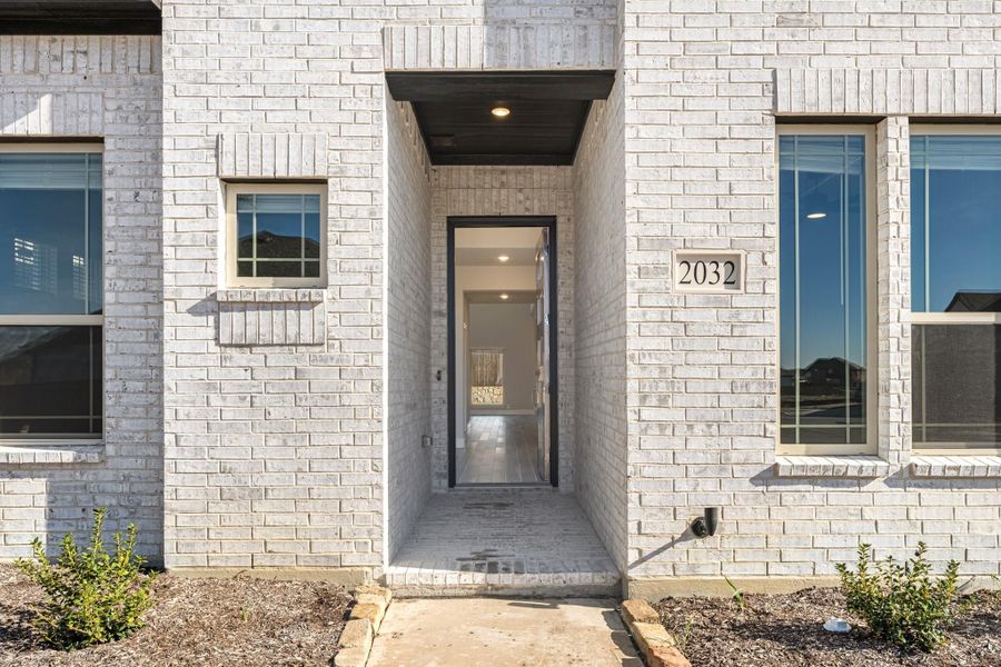 Front entry of home 2032 with white painted brick exterior, recessed covered doorway, and open front door Front entry of home 2032 with white painted brick exterior, recessed covered doorway, and open front door