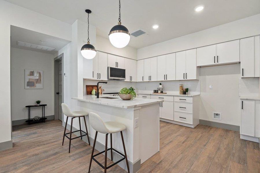 Kitchen featuring white cabinetry, backsplash, a breakfast bar, decorative light fixtures, and a peninsula
