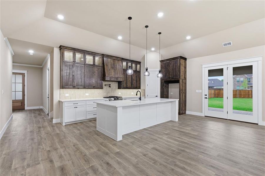 Open-concept kitchen featuring a large central island, two-tone cabinetry, wood-finish flooring, and double glass-paneled doors to the backyard Open-concept kitchen featuring a large central island, two-tone cabinetry, wood-finish flooring, and double glass-paneled doors to the backyard