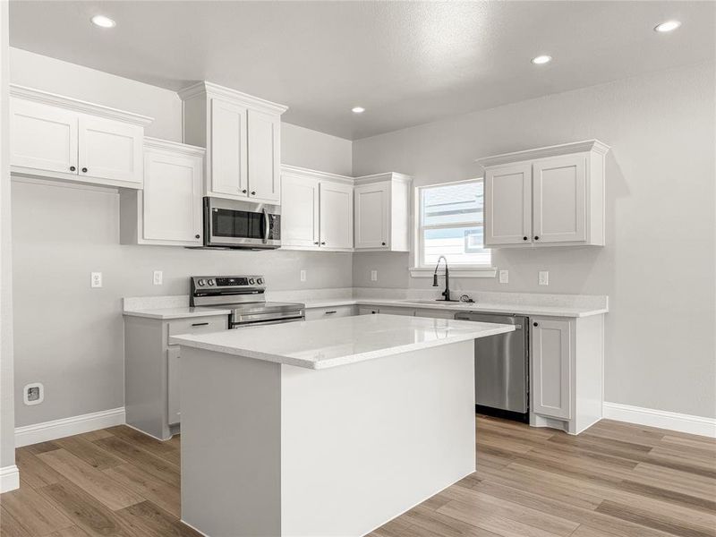Kitchen featuring a central island with white cabinetry, stainless steel appliances, wood-finish flooring, recessed lighting, and a window above the sink Kitchen featuring a central island with white cabinetry, stainless steel appliances, wood-finish flooring, recessed lighting, and a window above the sink