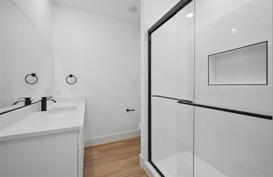 Full bath with double vanity, a shower stall, toilet, and wood finished floors