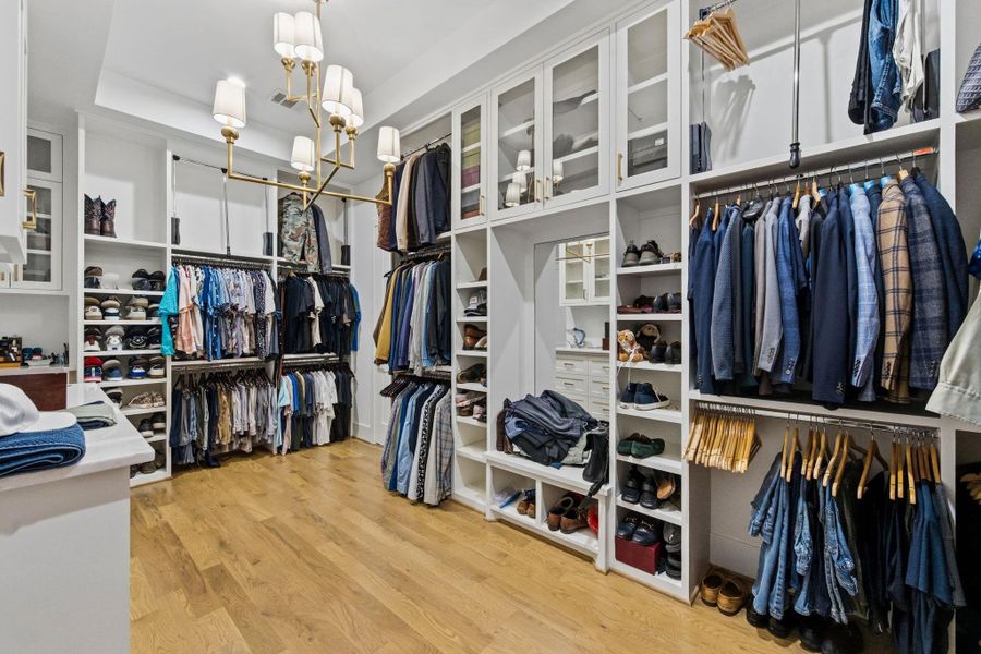 Oversized, custom-designed primary closet with built-ins, glass-front cabinetry, and ample storage—designed like a private boutique.