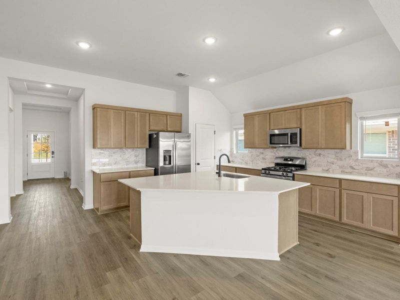 Kitchen featuring a central island with a sink, stainless steel appliances, wood-finish flooring, recessed lighting, and light-toned cabinetry with a patterned backsplash