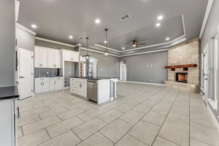 Kitchen with ceiling fan, dishwasher, an island with sink, a fireplace, and white cabinets