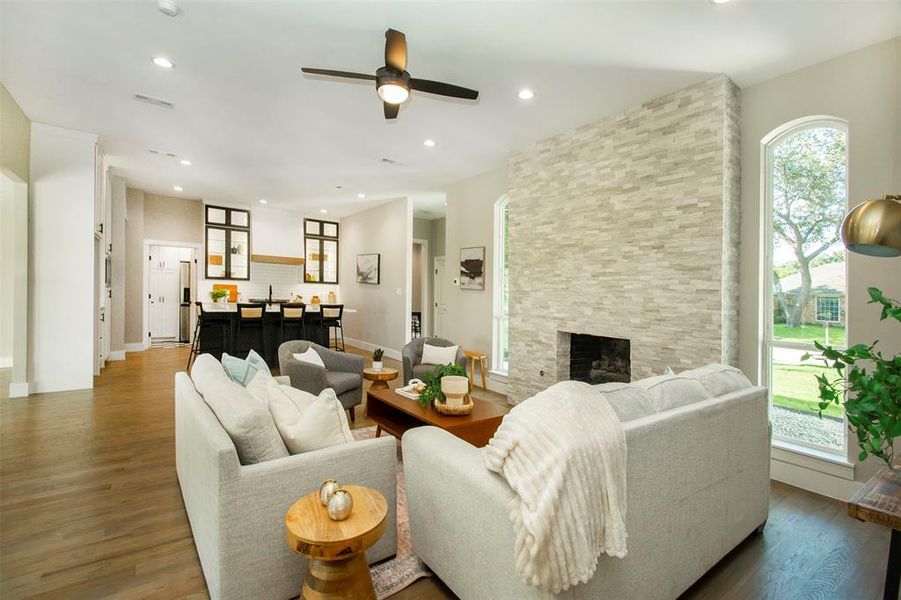 Living room featuring dark wood-type flooring, a healthy amount of sunlight, ceiling fan, and a stone fireplace