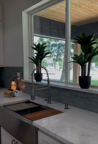 Kitchen sink area featuring a large window, stainless steel farmhouse sink with integrated cutting board, pull-down faucet, and white countertops
