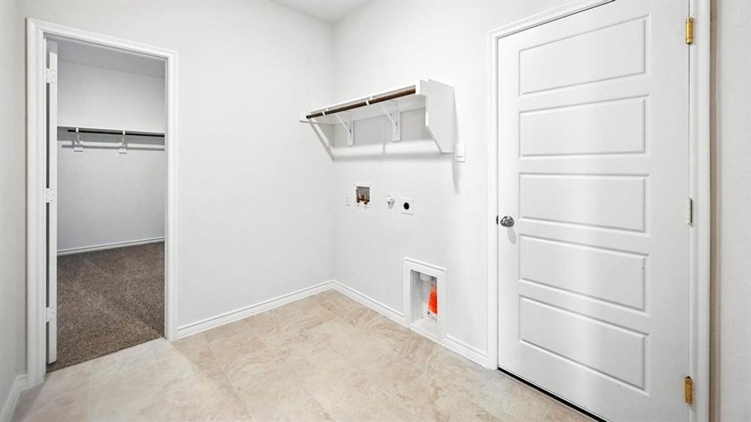 Utility room featuring light-toned tile flooring, white walls, and a built-in shelf with hanging rod