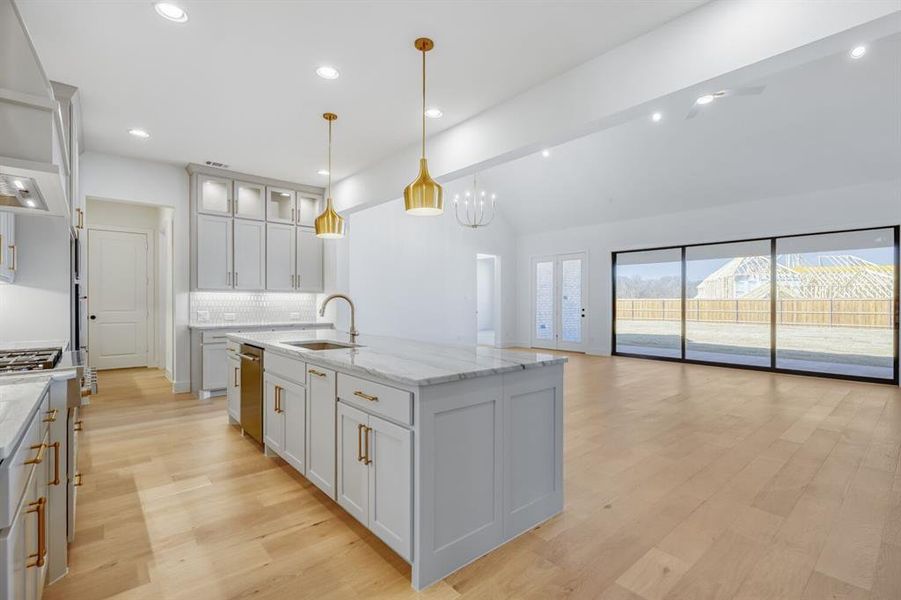Kitchen with vaulted ceiling with beams, light wood-style floors, glass fronted cabinets, light stone countertops, and open floor plan