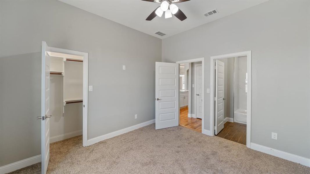 Unfurnished bedroom with ensuite bath, carpet, visible vents, and a walk in closet