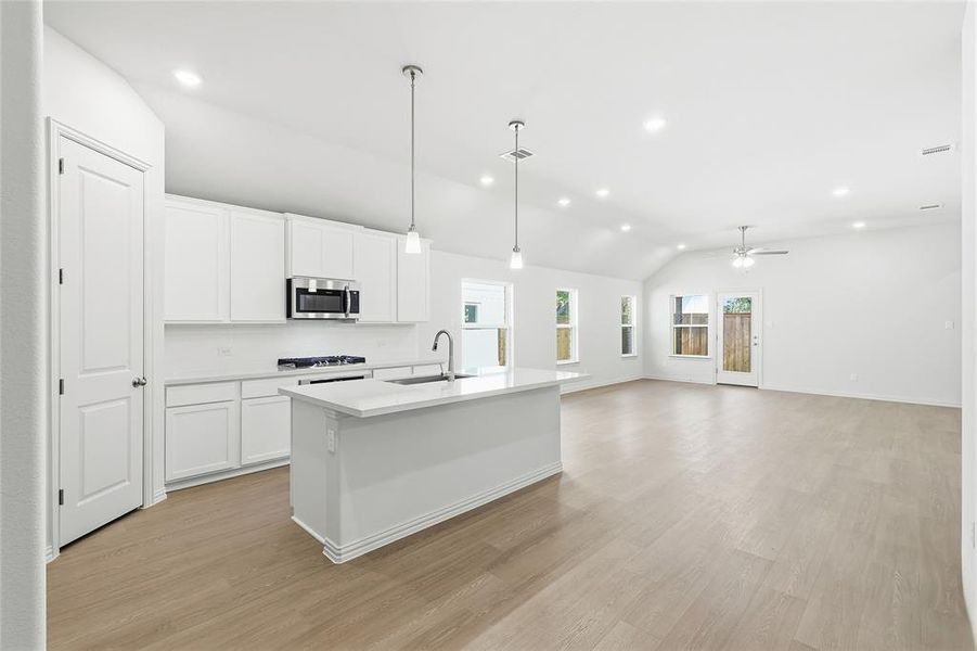 Kitchen featuring hanging light fixtures, lofted ceiling, recessed lighting, a kitchen island with sink, and white cabinets