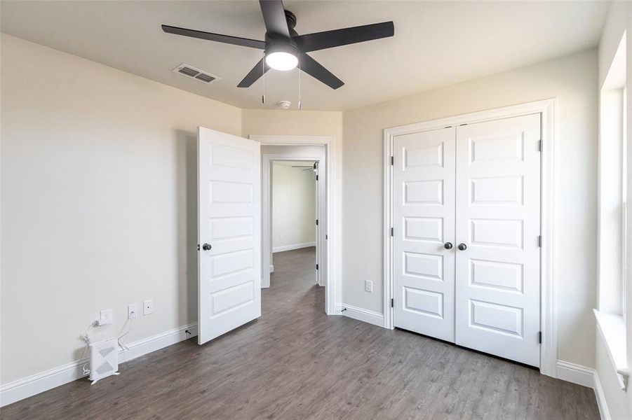 Interior room featuring wood-finish flooring, a contemporary ceiling fan, white paneled doors, and natural light from a window