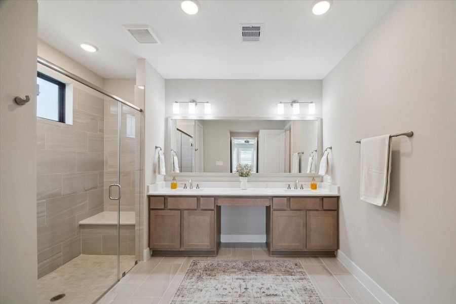 Spa-inspired bath featuring a large glass-enclosed shower with bench seating, dual vanities with generous storage, and a spacious layout that feels airy and refined.