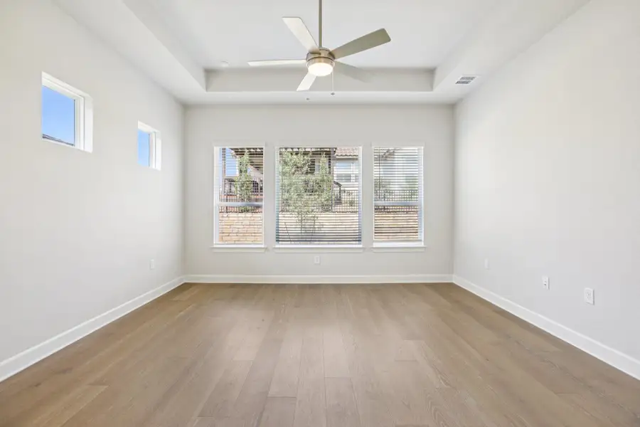 Unfurnished room with healthy amount of natural light, light wood finished floors, ceiling fan, and a tray ceiling