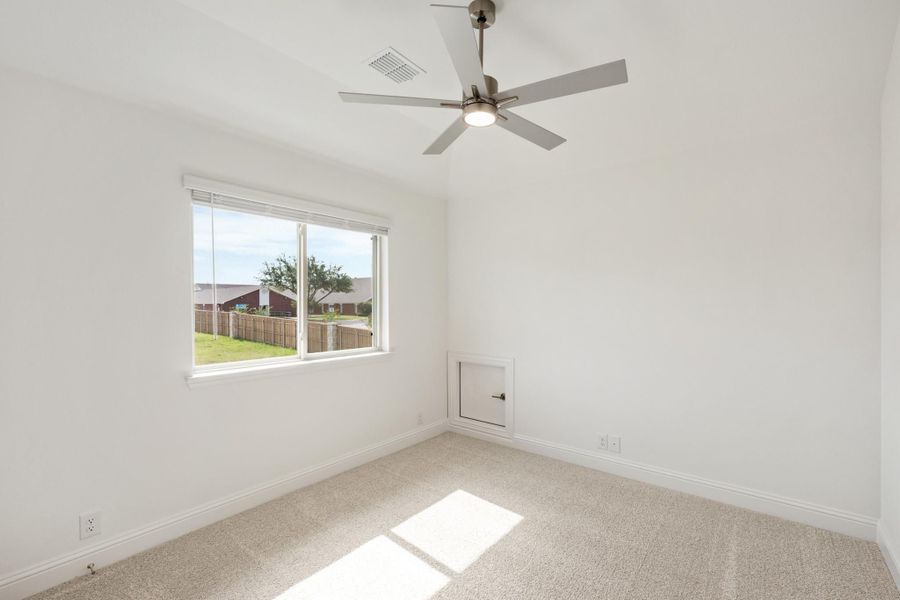 Empty bedroom with carpet, ceiling fan, and window overlooking a fenced backyard