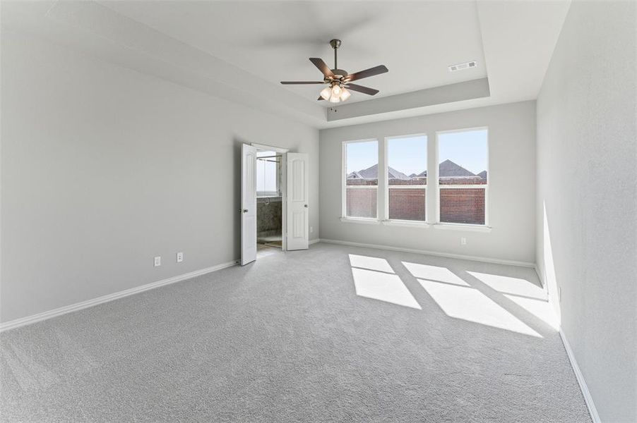 Unfurnished bedroom with a raised ceiling, carpet, a ceiling fan, and connected bathroom