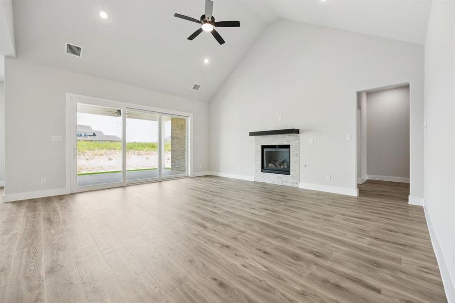 Unfurnished living room featuring high vaulted ceiling, recessed lighting, light wood finished floors, a ceiling fan, and a glass covered fireplace