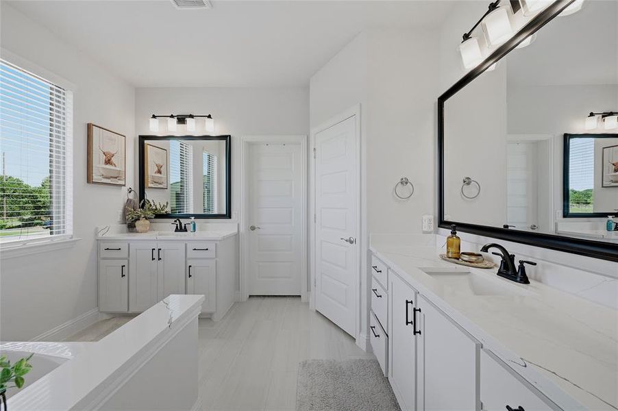 Spacious bathroom featuring dual vanities with white cabinetry, quartz countertops, and matte black fixtures