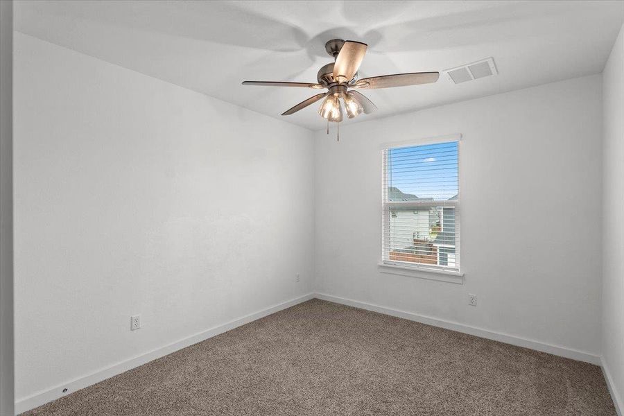 A well-lit bedroom features plush carpeting and a modern ceiling fan, offering comfortable living.