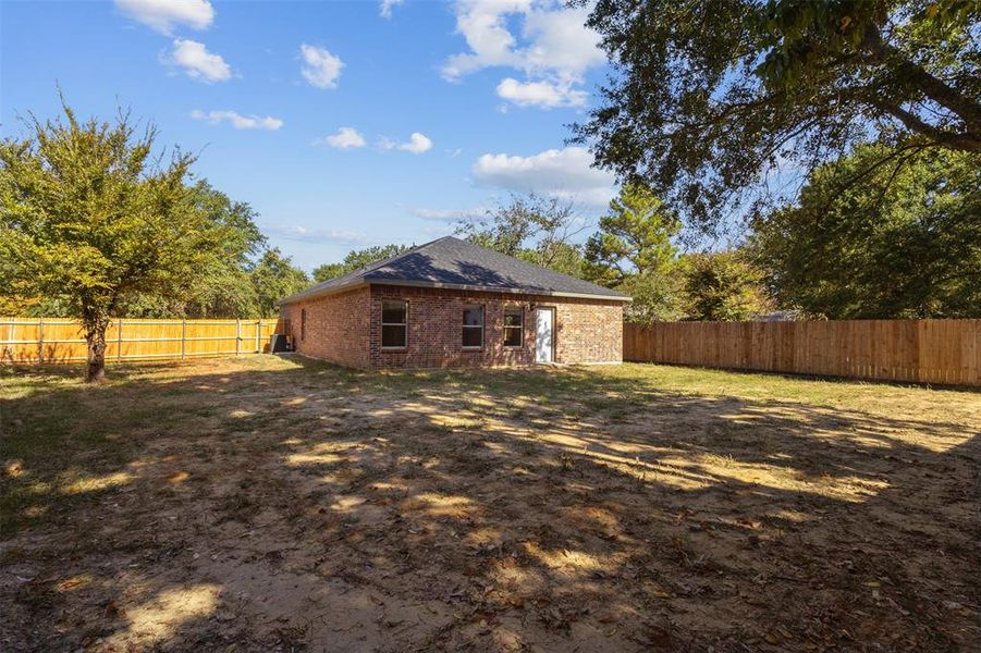 Back of property with a fenced backyard, brick siding, and a shingled roof Back of property with a fenced backyard, brick siding, and a shingled roof