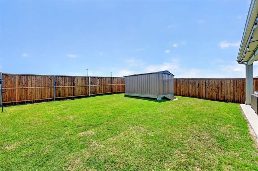 Expansive backyard featuring a lush green lawn, full wood privacy fencing, and a large metal storage shed