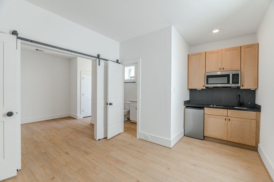 This photo shows a compact kitchen with light wood cabinetry, a small fridge, microwave, and sink. Adjacent is a room with sliding doors and light wood flooring, leading to a bathroom. The space is modern and bright.Photo Disclaimer: Photos are representative of the community and may depict a similar floor plan, model home, or previously completed residence. This photo shows a compact kitchen with light wood cabinetry, a small fridge, microwave, and sink. Adjacent is a room with sliding doors and light wood flooring, leading to a bathroom. The space is modern and bright.Photo Disclaimer: Photos are representative of the community and may depict a similar floor plan, model home, or previously completed residence.
